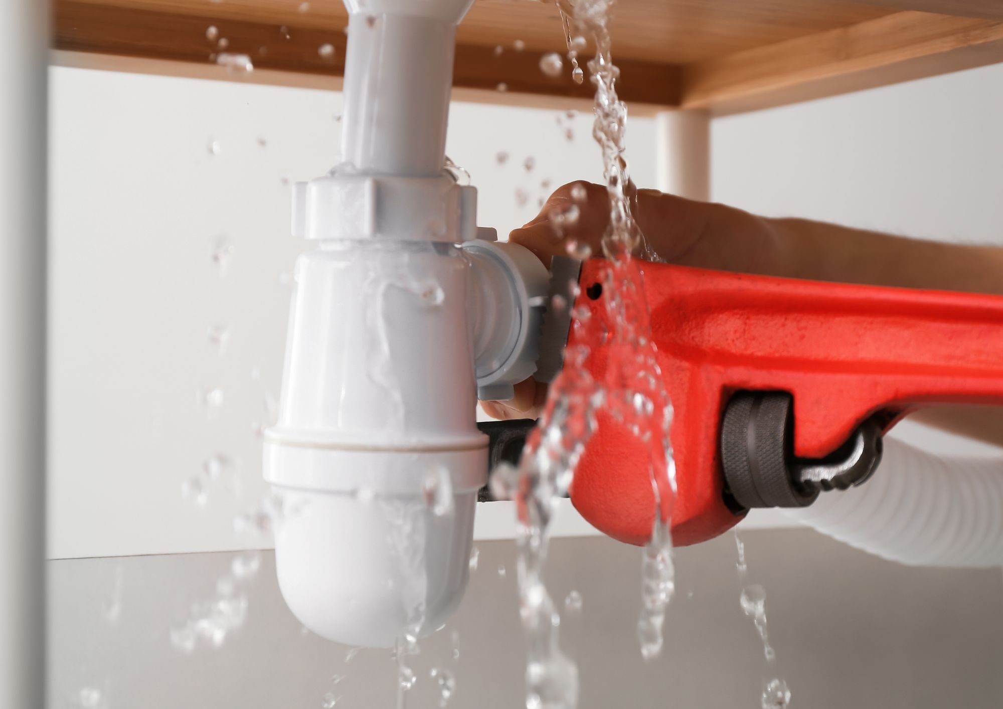Plombier réparant une conduite d'eau avec une clé à tuyau rouge sous un siphon blanc